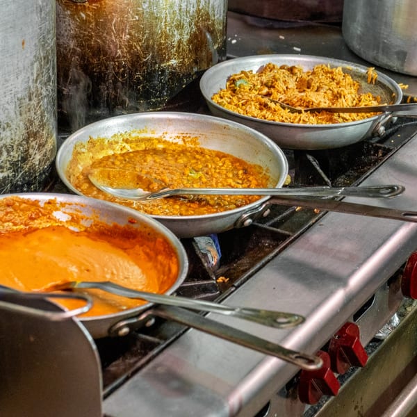 Three pans of Indian food, including rice, dal, and a red curry, cooking on a stove.