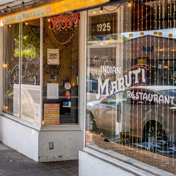 Exterior of Maruti Indian Restaurant with a yellow awning, window decals, and string lights.