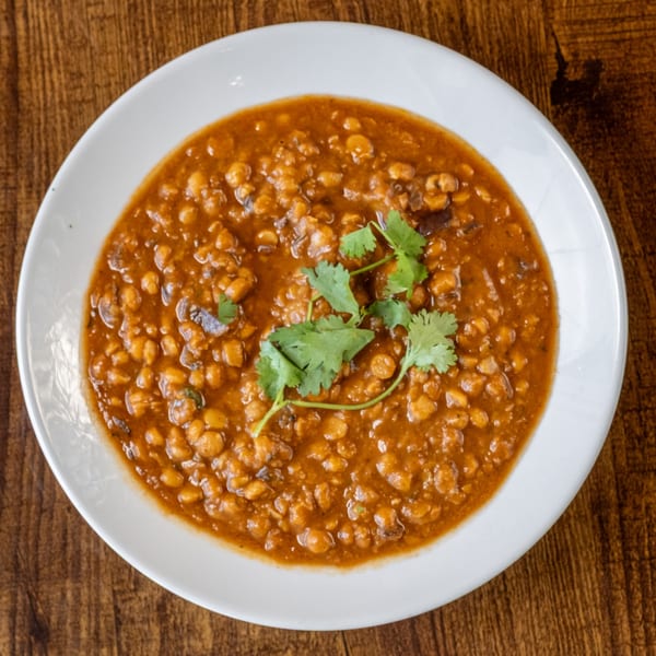 A white bowl of Maruti Indian Restaurant's chana masala, garnished with fresh cilantro, on a wooden table.