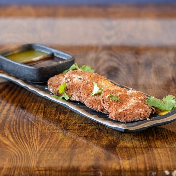 Maruti Indian Restaurant's crispy brown patties with cilantro garnish and dipping sauces on a dark plate.