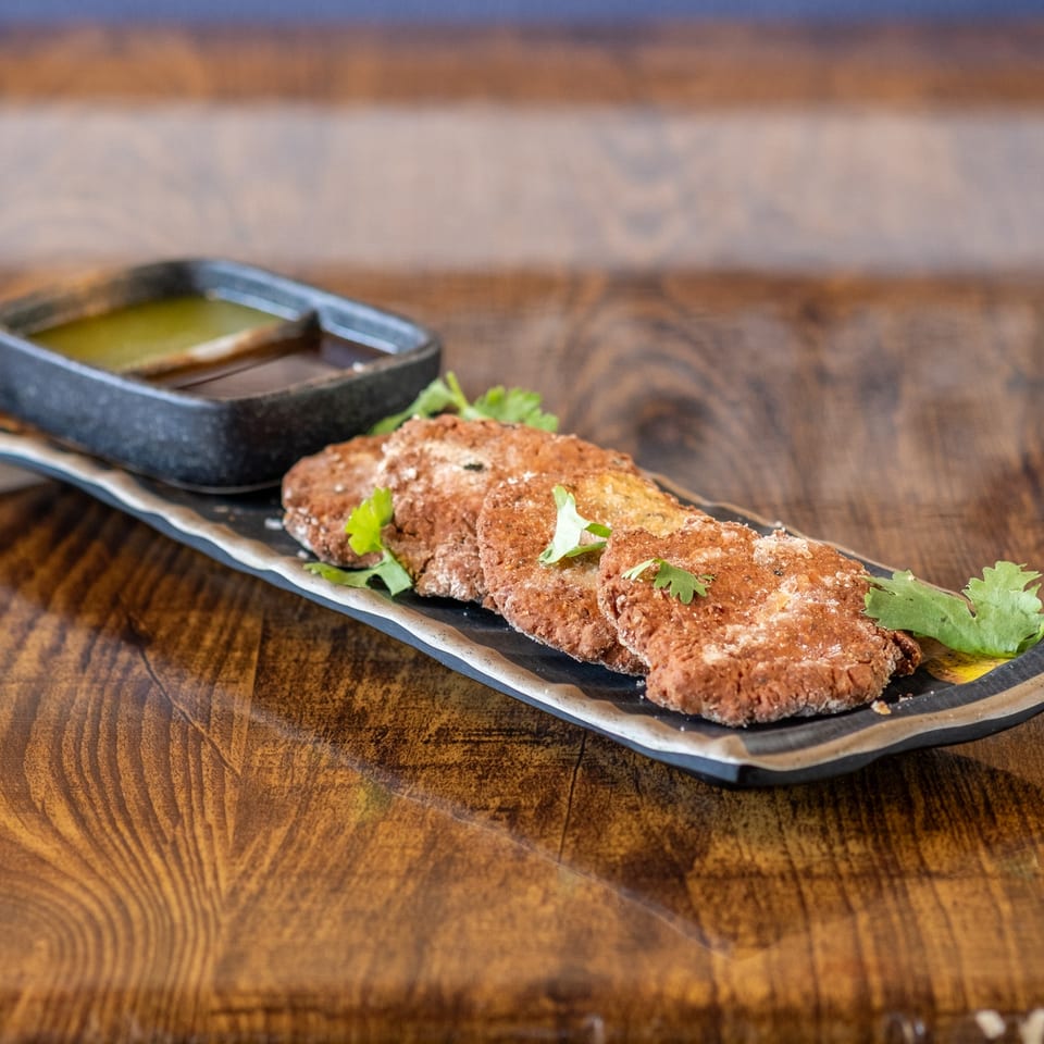 Maruti Indian Restaurant's crispy brown patties with cilantro garnish and dipping sauces on a dark plate.