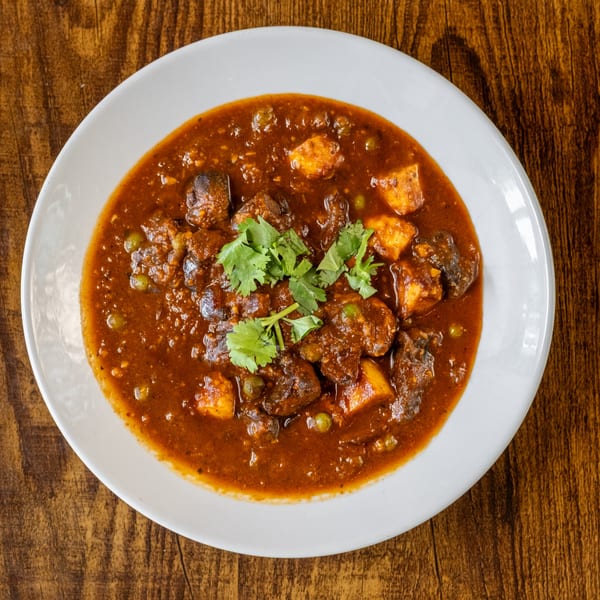 A white bowl of Maruti Indian Restaurant's paneer and mushroom curry, garnished with fresh cilantro.