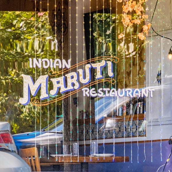 Maruti Indian Restaurant sign on a window, adorned with string lights and reflecting trees.