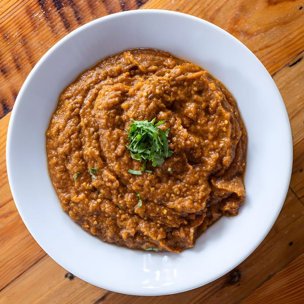 A white bowl of Maruti Indian Restaurant's brown, textured curry, garnished with fresh green herbs.