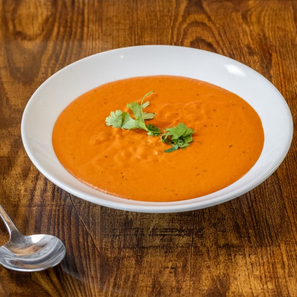 A white bowl of vibrant orange Indian curry, garnished with fresh cilantro, on a wooden table.